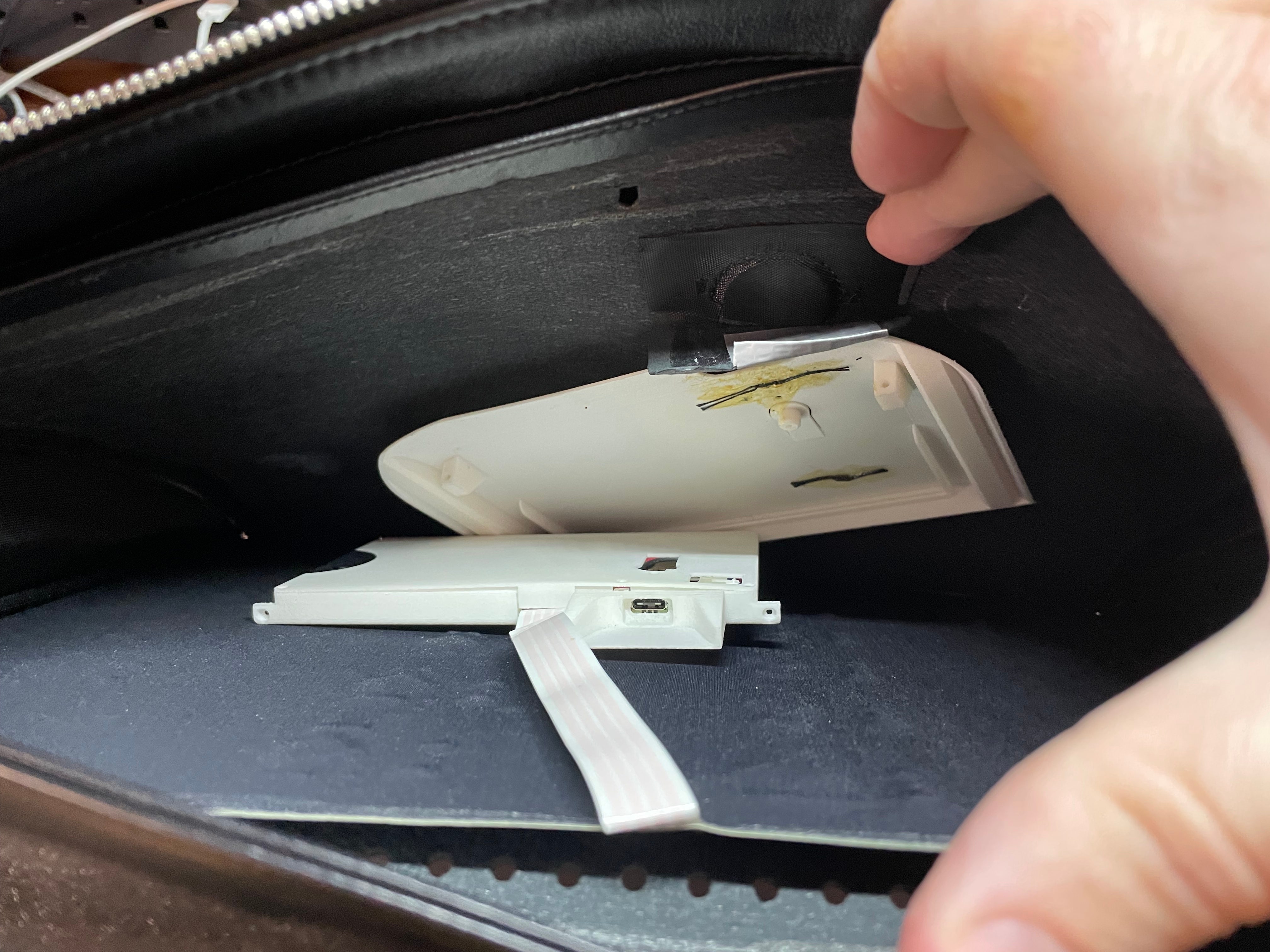 Inside of the flap concealing the electronics, showing the LED panel covered with black fabric against the front of the bag, ribbon cable going from the top of the panel into the 3D-printed controller board case, and the 3D-printed outer shell which is sewn to the back of the flap.